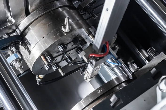 Un macchinario industriale con testa cirolare sta lavorando degli articoli tecnici in plastica cilindrici.