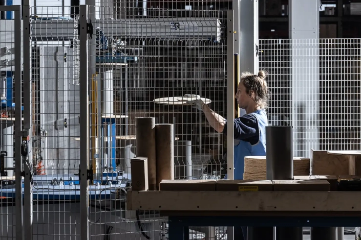 Monplast-8248-1500×1000 The interior of a factory with a detail of an operator loading a circular plywood piece onto a machine to produce a reel for industrial electric cables.