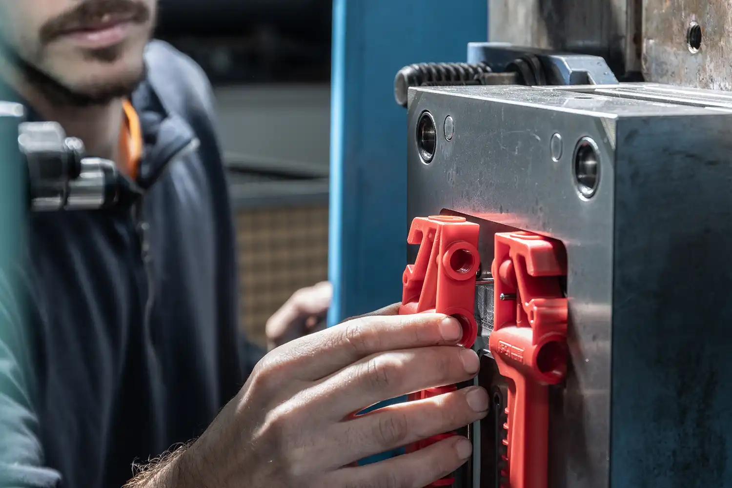 Un operatore che tocca un articolo tecnico in plastica rossa inserita in un macchinario.